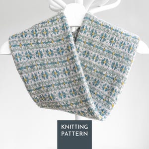 May include: A knitted cowl featuring a fair isle pattern in shades of light gray, teal, and mustard yellow. The accessory is displayed on a white hanger and includes a dark gray square graphic at the bottom with the text KNITTING PATTERN.