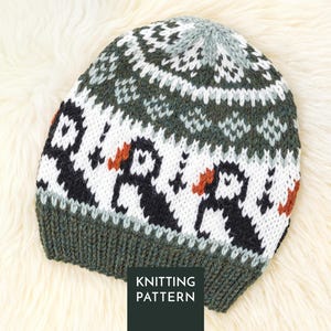 May include: A knitted beanie featuring a repeating pattern of black and white puffins with orange beaks against a white background, bordered by dark green ribbed trim and a dark green and white geometric design at the crown. Text reads KNITTING PATTERN.