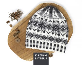 Könnte beinhalten: Eine gestrickte Mütze mit einem Fair-Isle-Muster in Weiß, Hellgrau, Dunkelgrau und Schwarz. Die Mütze hat ein sich wiederholendes geometrisches Design und einen gestreiften Rand an der Basis. Ein dunkelgraues Quadrat mit dem Text KNITTING PATTERN ist sichtbar.