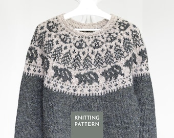 May include: A long-sleeved knit jumper featuring a dark charcoal grey body and a lighter beige yoke. The yoke displays a detailed fair isle pattern with dark grey silhouettes of pine trees and bears. A grey box with the text KNITTING PATTERN is visible.