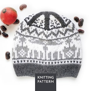 Può includere: Un berretto lavorato a maglia con un motivo jacquard nei colori bianco, grigio chiaro e grigio scuro. Il design include motivi di renne stilizzate, forme geometriche e un bordo a coste grigio scuro. Il testo KNITTING PATTERN è visibile.