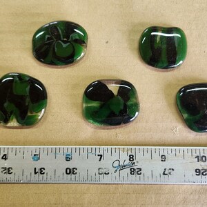 May include: Five green and black glass cabochons with a marbled effect. The cabochons are oval shaped and have a glossy finish.