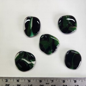 May include: Five green, black, and white glass stones with an irregular shape. The stones are smooth and glossy.