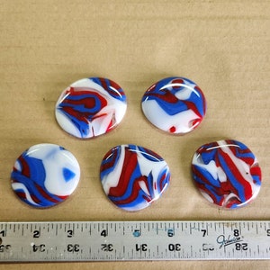 May include: Five round glass cabochons with a swirling red, white, and blue pattern. The cabochons are approximately 1 inch in diameter.