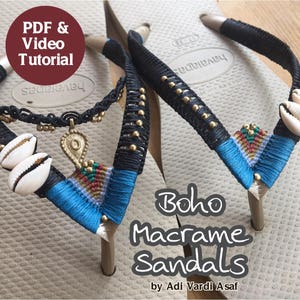 Op de afbeelding: Een paar beige slippers met zwarte en blauwe macramé-versieringen. De macramé bevat kleine witte schelpen en een gouden hanger. De tekst "Boho Macrame Sandals" en "by Adi Vardi Asaf" staat op de slippers.