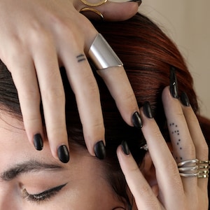 May include: A person wearing multiple silver rings on their fingers. The rings are simple and modern in design. The person has black nail polish on their nails.