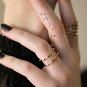 May include: Two gold rings with a bamboo-like design. The rings are stacked on each other and worn on a finger.