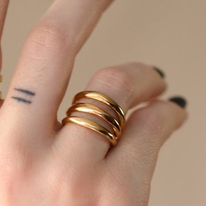 Puede incluir: Un anillo de oro con cuatro bandas apiladas una encima de la otra. El anillo se lleva en un dedo.
