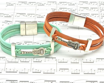 May include: Two leather bracelets with guitar charm accents. One bracelet is brown and the other is mint green.