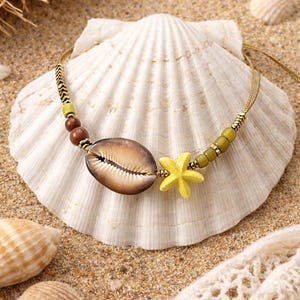 Op de afbeelding: Een ketting met strandthema met een grote, bruine en beige zeeschelpenhanger, een gele zeesterbedel en bruine en groene kralen. De ketting wordt gepresenteerd op een grote, witte zeeschelp, wat een kustesthetiek creëert.