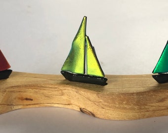 Könnte beinhalten: Drei Miniatur-Segelschiffe aus Glas, jedes mit einem anderen Segel in der Farbe: Rot, Grün und Gelb. Die Segelschiffe werden auf einem Holzsockel präsentiert.