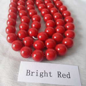May include: A strand of bright red round beads. The beads are smooth and glossy. The beads are arranged in a row, with the text "Bright Red" written on a white label below.