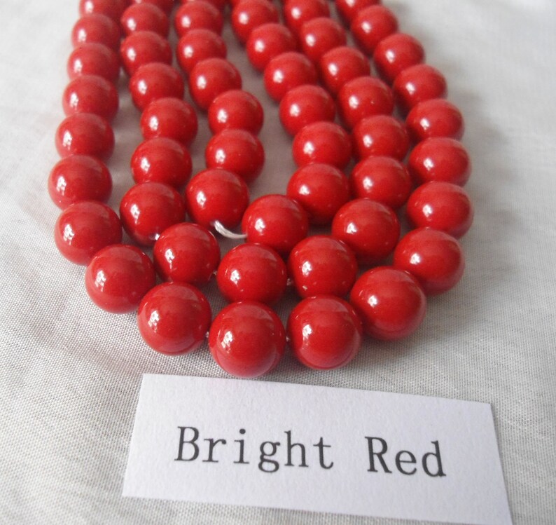 May include: A strand of bright red round beads. The beads are smooth and glossy. The beads are arranged in a row, with the text "Bright Red" written on a white label below.