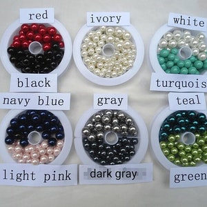 May include: Assortment of pearl beads in various colors, including red, ivory, white, turquoise, teal, navy blue, gray, light pink, dark gray, and green. The beads are displayed in small white containers with labels indicating their color.