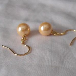 May include: A pair of gold tone earrings with a large, round, cream-colored pearl on each earring.
