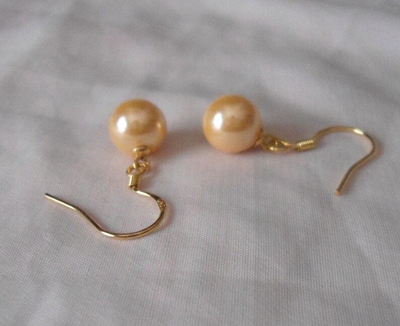 May include: A pair of gold tone earrings with a large, round, cream-colored pearl on each earring.