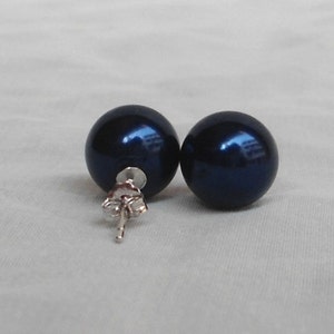 May include: A pair of dark blue, spherical stud earrings. The earrings have a shiny, reflective surface and are set on silver posts with butterfly backs. The earrings are displayed on a white surface.