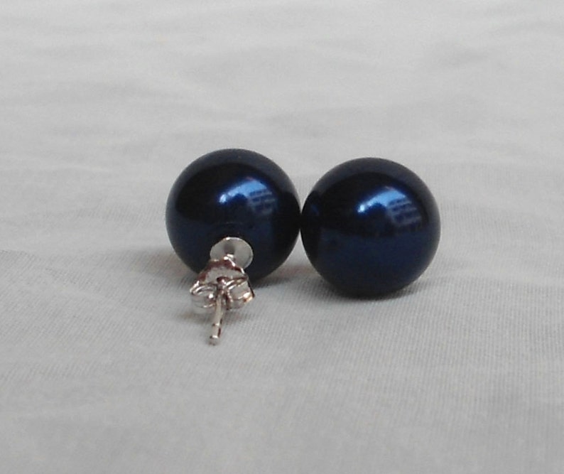 May include: A pair of dark blue, spherical stud earrings. The earrings have a shiny, reflective surface and are set on silver posts with butterfly backs. The earrings are displayed on a white surface.
