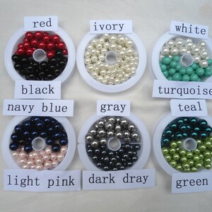 May include: An assortment of colorful beads in various shades, including red, black, ivory, white, turquoise, teal, navy blue, light pink, gray, dark gray, and green. Each color is labeled on a white tag. These beads are likely for jewelry making or crafting.