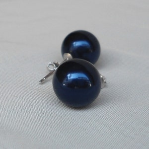 May include: A pair of dark blue, spherical stud earrings. The earrings have a glossy finish and are set on silver posts. The earrings are displayed on a light gray fabric background.