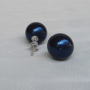 May include: A pair of dark blue, spherical stud earrings. The earrings have a glossy finish and are set on silver posts with butterfly clasps. The earrings are displayed on a light-colored, textured surface.