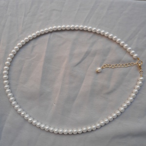 May include: A white pearl necklace with a gold clasp. The necklace is made of small, round pearls and is about 18 inches long.