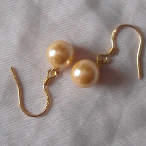 May include: A pair of gold tone earrings with a large, round, peach-colored pearl on each earring.