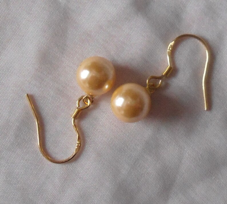 May include: A pair of gold tone earrings with a large, round, peach-colored pearl on each earring.