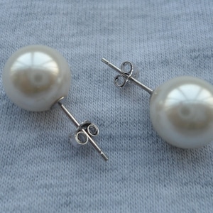 May include: A pair of white pearl stud earrings with silver posts and butterfly backs.