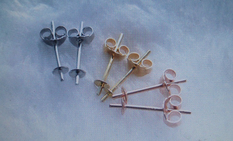 May include: An assortment of earring posts in silver, gold, and rose gold tones. The posts have a flat disc at the base for attaching earrings and a butterfly clutch backing. The earrings are displayed on a light blue background.