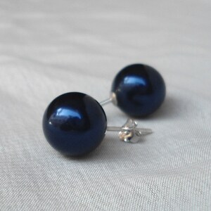 May include: A pair of dark navy blue stud earrings. Each earring features a large, round, glossy bead. The earrings have silver-colored posts and butterfly backs. The earrings are set against a light background.