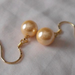 May include: A pair of gold earrings with a light peach colored pearl on each earring.