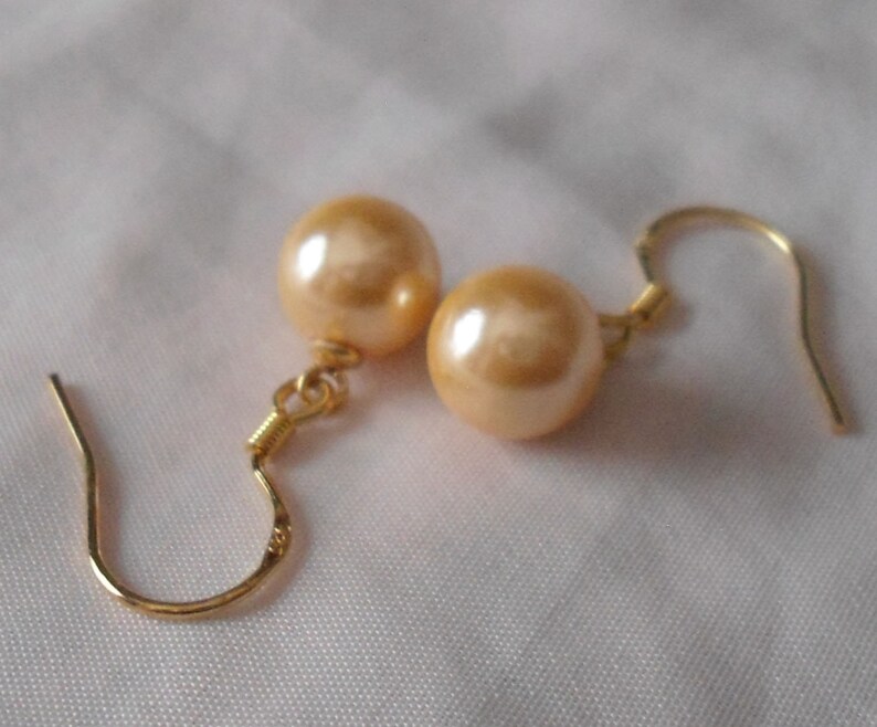 May include: A pair of gold earrings with a light peach colored pearl on each earring.