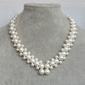 Puede incluir: Un collar de perlas blancas con un diseño en forma de V. El collar está hecho de pequeñas perlas redondas que están enhebradas en un alambre.
