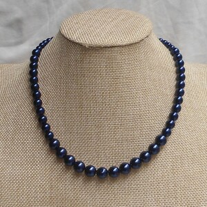 May include: A dark blue pearl necklace on a brown fabric mannequin.