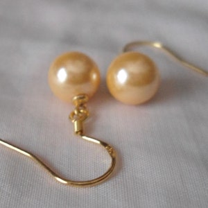 May include: A pair of gold tone earrings with a single large, round, cream-colored pearl on each earring.