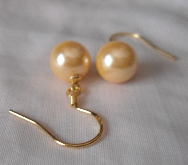 May include: A pair of gold tone earrings with a single large, round, cream-colored pearl on each earring.