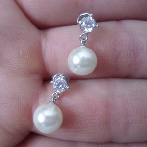 May include: A pair of silver earrings with a small clear rhinestone and a white pearl drop.