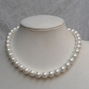 May include: A white pearl necklace on a white mannequin bust. The necklace is made of round, smooth pearls.