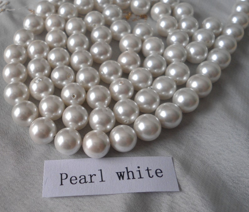 May include: A strand of white pearl beads. The beads are round and smooth, and they are arranged in a loose, flowing pattern. The beads are all the same size, and they are strung on a clear thread. The beads are arranged in a loose, flowing pattern. The beads are all the same size, and they are strung on a clear thread. The text "Pearl white" is written on a white card.