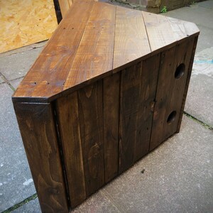 May include: A dark brown wooden corner TV stand with a triangular top and two holes on the side. The stand is made of reclaimed wood planks.