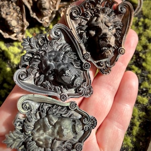May include: Ornate, antique-style lion head embellishments in various shades of bronze and silver. The lion heads are framed with decorative scrollwork and floral accents. The image showcases several of these detailed, vintage-inspired decorative elements.