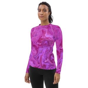 May include: A long-sleeved shirt with a vibrant, swirling pattern in shades of pink and purple. The shirt has a crew neck and white stitching along the seams. The model is wearing black leggings.