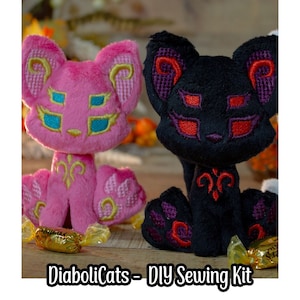 May include: A DIY sewing kit featuring two plush cat plushies. One cat is pink with gold embroidery and blue eyes, the other is black with red and purple embroidery and red eyes. The kit is called "DiaboliCats".