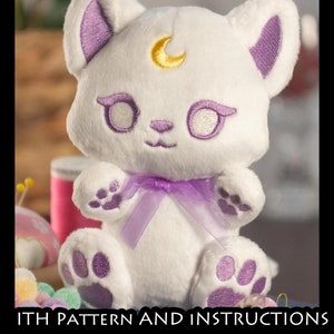 May include: White plush cat with purple ears, paws, and a purple bow. The cat has a gold crescent moon on its forehead and embroidered eyes.