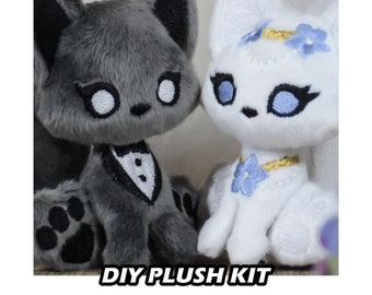 May include: DIY plush kit featuring two adorable fox plushies. The gray fox is wearing a tuxedo and the white fox is wearing a white dress with blue flowers.  "DIY Plush Kit" is written in white letters on a black background.