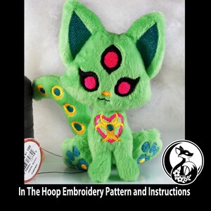 May include: Green plush cat with a third eye and a heart-shaped design on its chest. The cat has a long tail with yellow and green circles.
