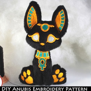 May include: Black plush toy of the Egyptian god Anubis, a jackal-headed deity, with gold and teal embroidery details. The toy is sitting with its paws visible.