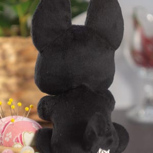 May include: Black plush toy in the shape of a dog sitting on a table. The toy has a small tail and a tag on its back that says "Carousel Customs".