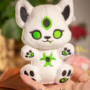 May include: White plush toy with green eyes and a black nose. The toy has a green biohazard symbol on its chest and black paw prints on its feet.